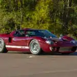 Seitenansicht eines roten 1965 Ford GT40 MkI auf offener Straße mit weißem Zierstreifen.