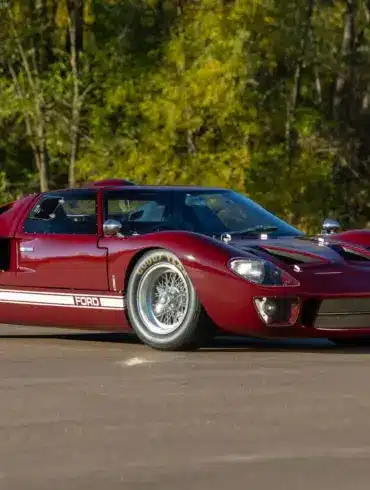 Seitenansicht eines roten 1965 Ford GT40 MkI auf offener Straße mit weißem Zierstreifen.