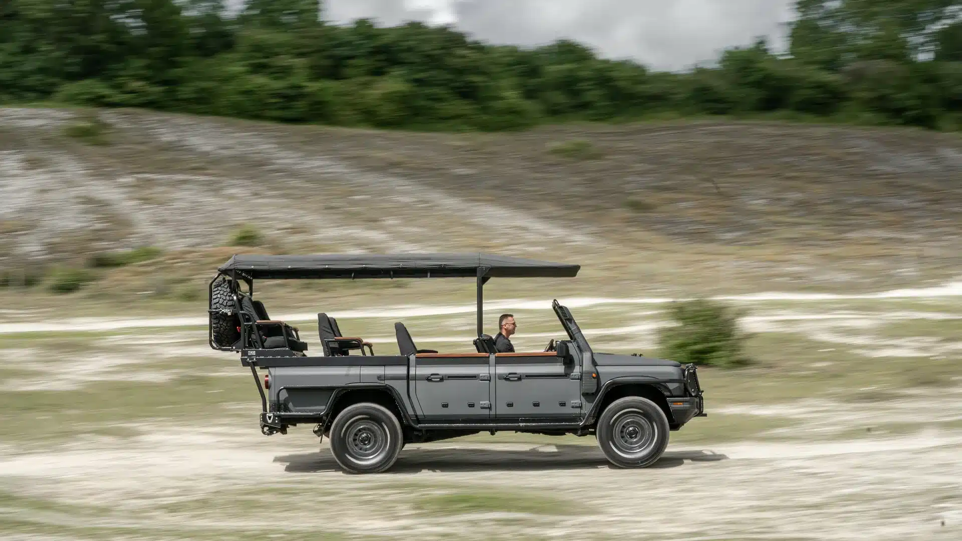 INEOS Grenadier Game Viewer als Offroad-Safari-Fahrzeug mit offenem Dach und Sitzreihen, fährt über sandigen Untergrund