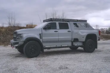 2020 International CV515 Pickup in Nardo-Grau mit Expeditionsausstattung, großen Offroad-Reifen und robusten Anbauteilen auf einem Kiesplatz.