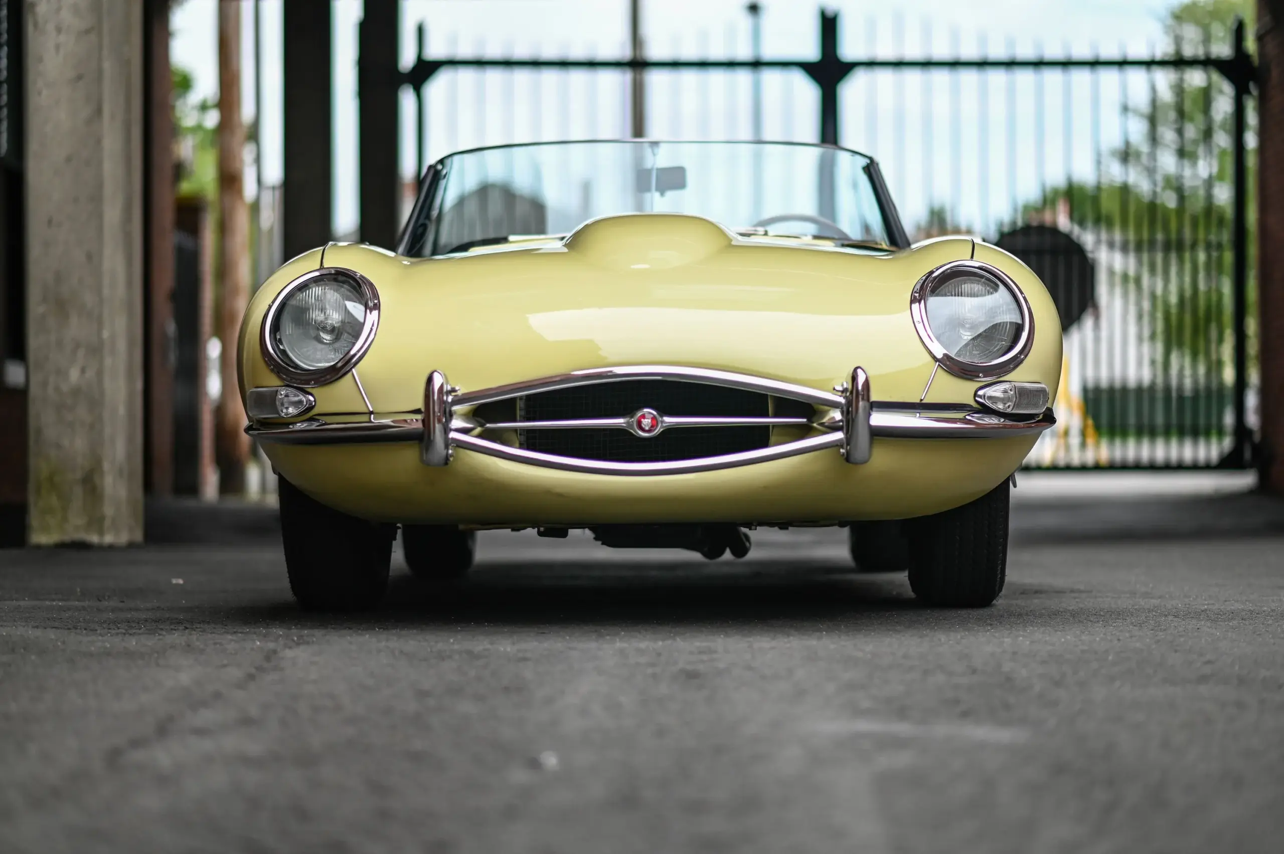 Frontale Aufnahme eines hellgelben Jaguar E-Type Series 1 Roadsters von 1967 mit Chromstoßfängern und geschlossenem Scheinwerferglas.