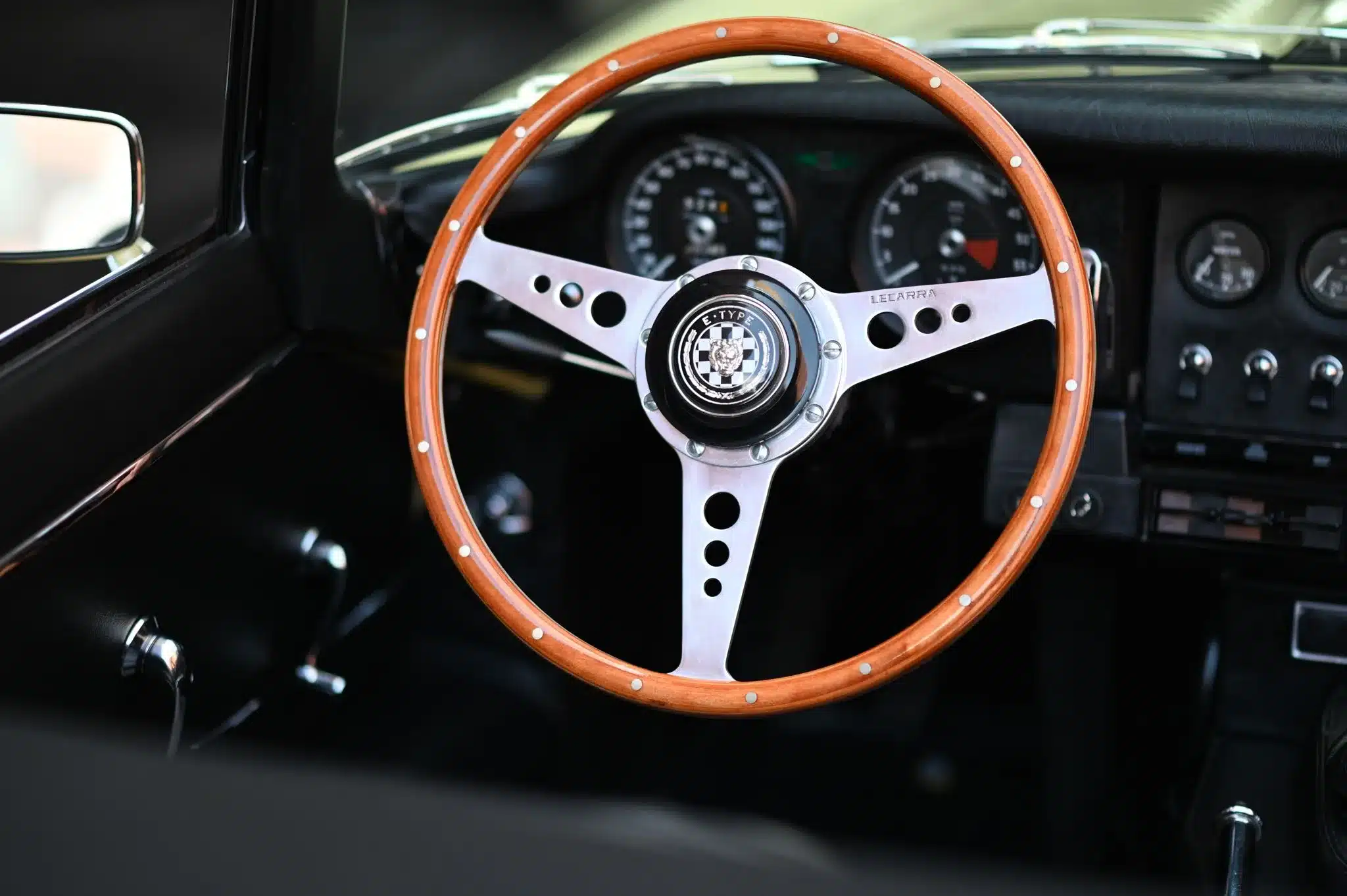 Nahaufnahme des Lecarra-Holzlenkrads und Armaturenbretts eines Jaguar E-Type Series 1 Roadster von 1967 mit klassischen Rundinstrumenten.