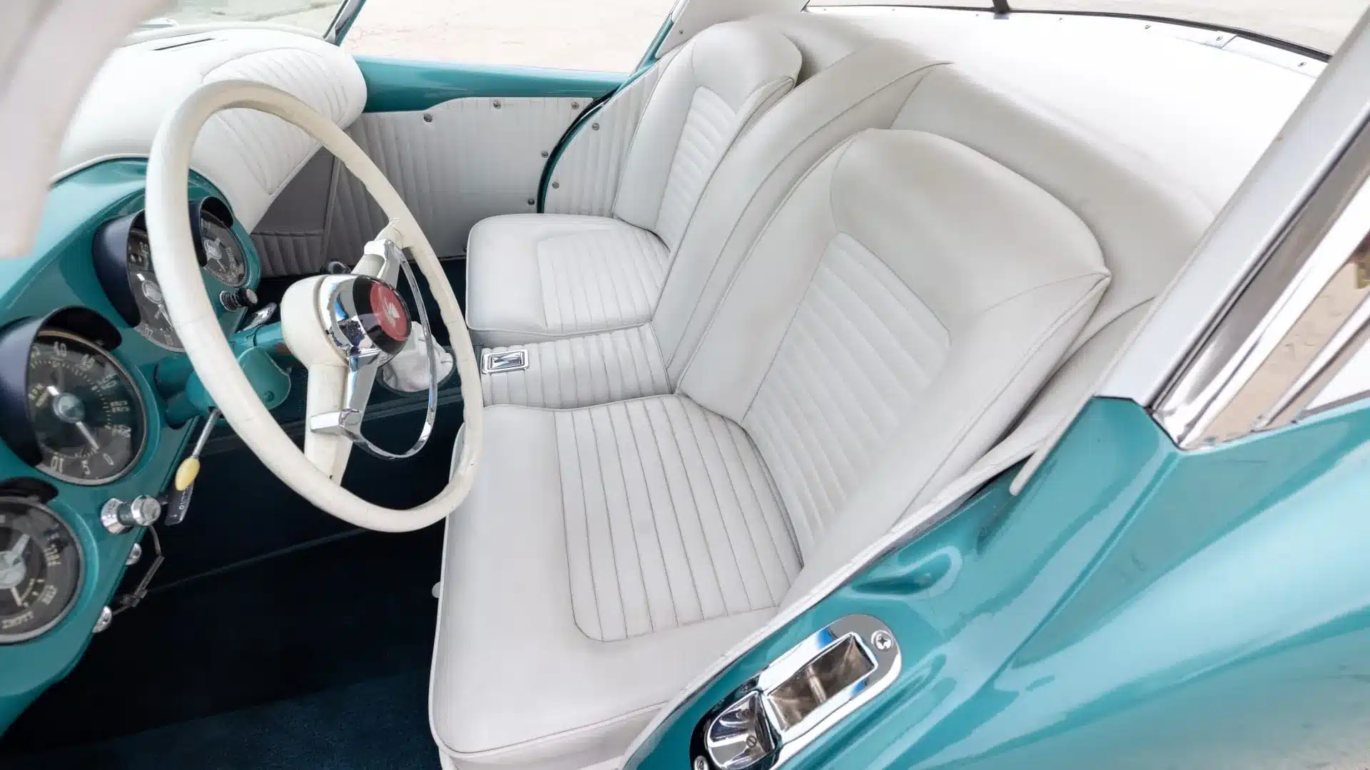 Nahaufnahme des Innenraums eines Kaiser Darrin 1954 mit cremefarbenen Sitzen und türkisfarbenem Armaturenbrett.