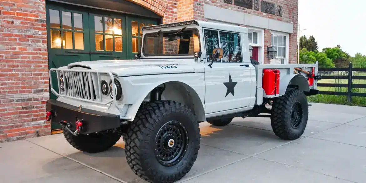 Komplett restaurierter Kaiser-Jeep M715 mit Offroad-Reifen, grauer Lackierung und modernen Ausstattungsdetails, abgestellt vor einem Backsteingebäude.