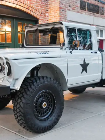 Komplett restaurierter Kaiser-Jeep M715 mit Offroad-Reifen, grauer Lackierung und modernen Ausstattungsdetails, abgestellt vor einem Backsteingebäude.