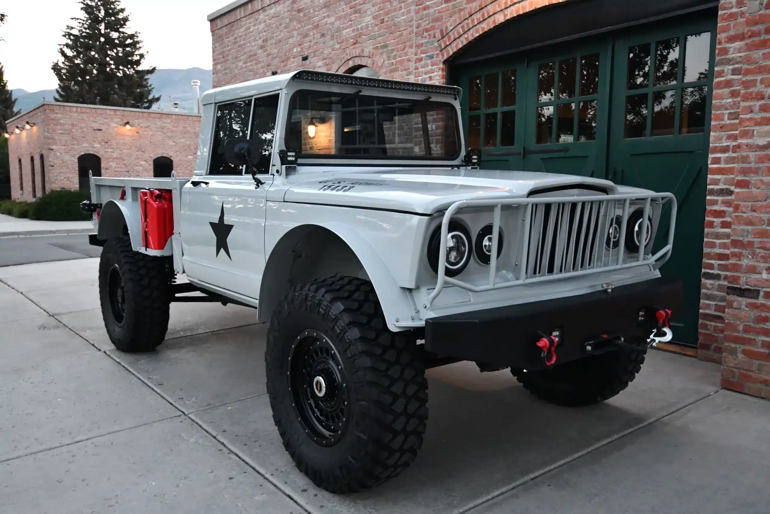 Restaurierter und modernisierter Kaiser-Jeep M715 ANV-KJ1 mit großen Offroad-Reifen und militärischem Dekor vor Garagentor