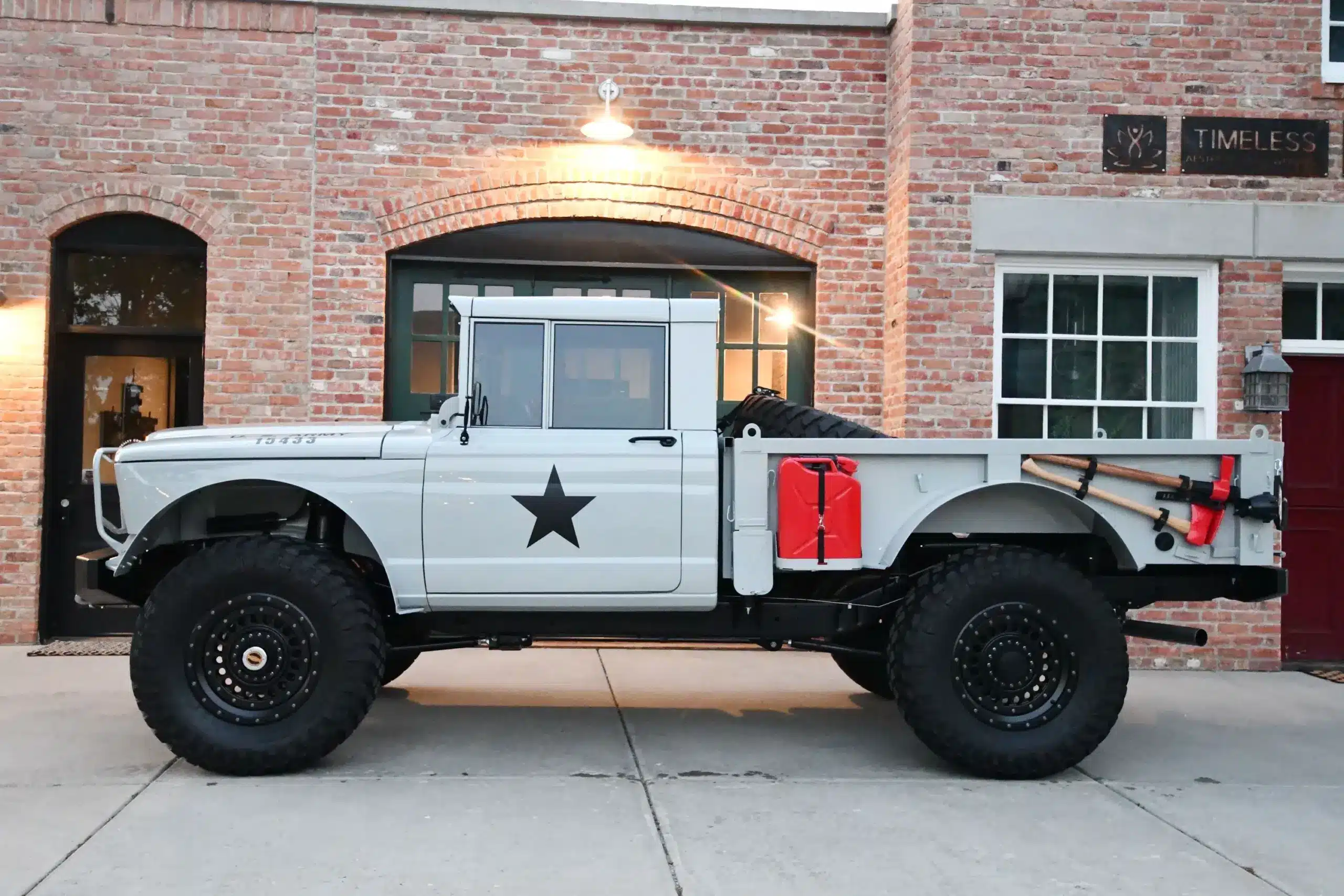 Komplett restaurierter Kaiser-Jeep M715 mit modernen Offroad-Komponenten, lackiert in Military Gray, vor einem Gebäude geparkt.