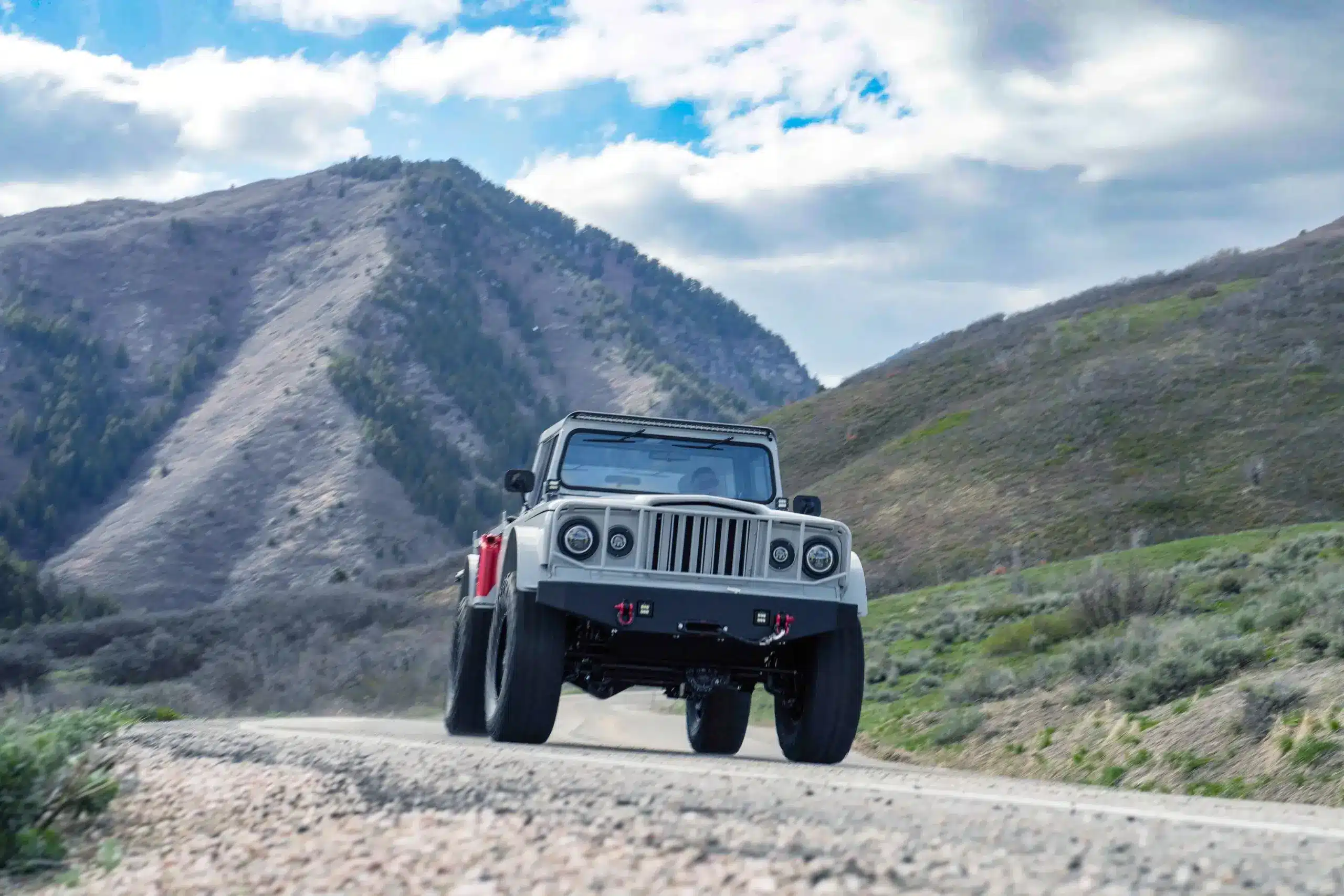 Modernisierter Kaiser-Jeep M715 fährt auf einer Straße vor einer Berglandschaft