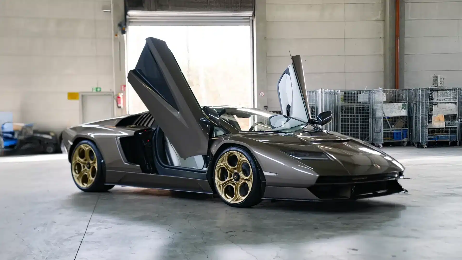 Lamborghini Countach LPI 800-4 in brauner Lackierung mit geöffneten Scherentüren und goldenen Felgen im Innenraum einer Halle.