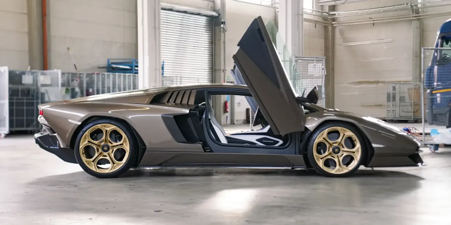 Lamborghini Countach LPI 800-4 in Luci del Bosco, Seitenansicht mit geöffneten Scherentüren und bronzenen Felgen in einer Werkstatthalle.