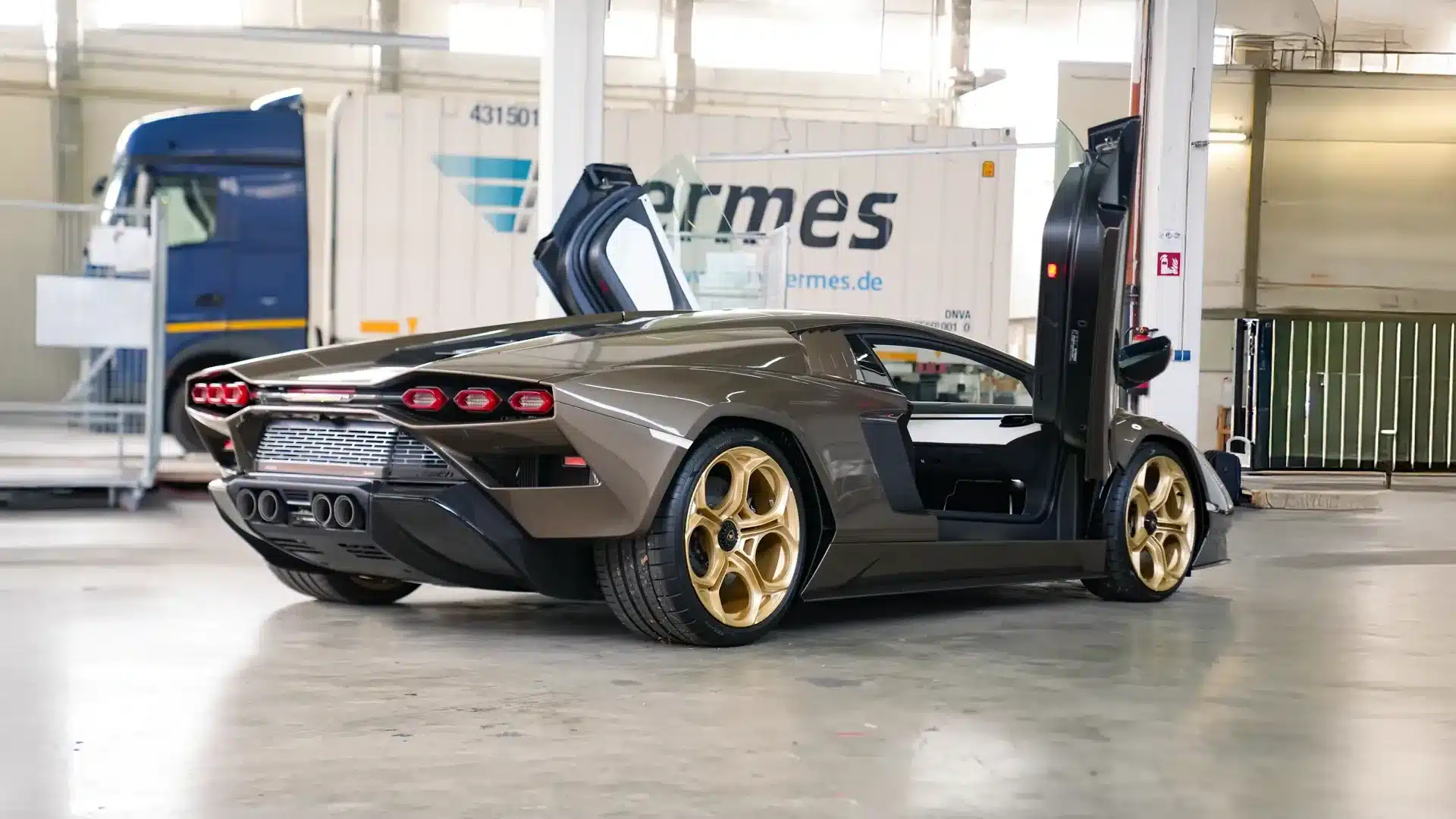 Lamborghini Countach LPI 800-4 in der Farbe Luci del Bosco mit offenen Scherentüren und goldenen Felgen, seitliche Heckansicht in einer Halle.