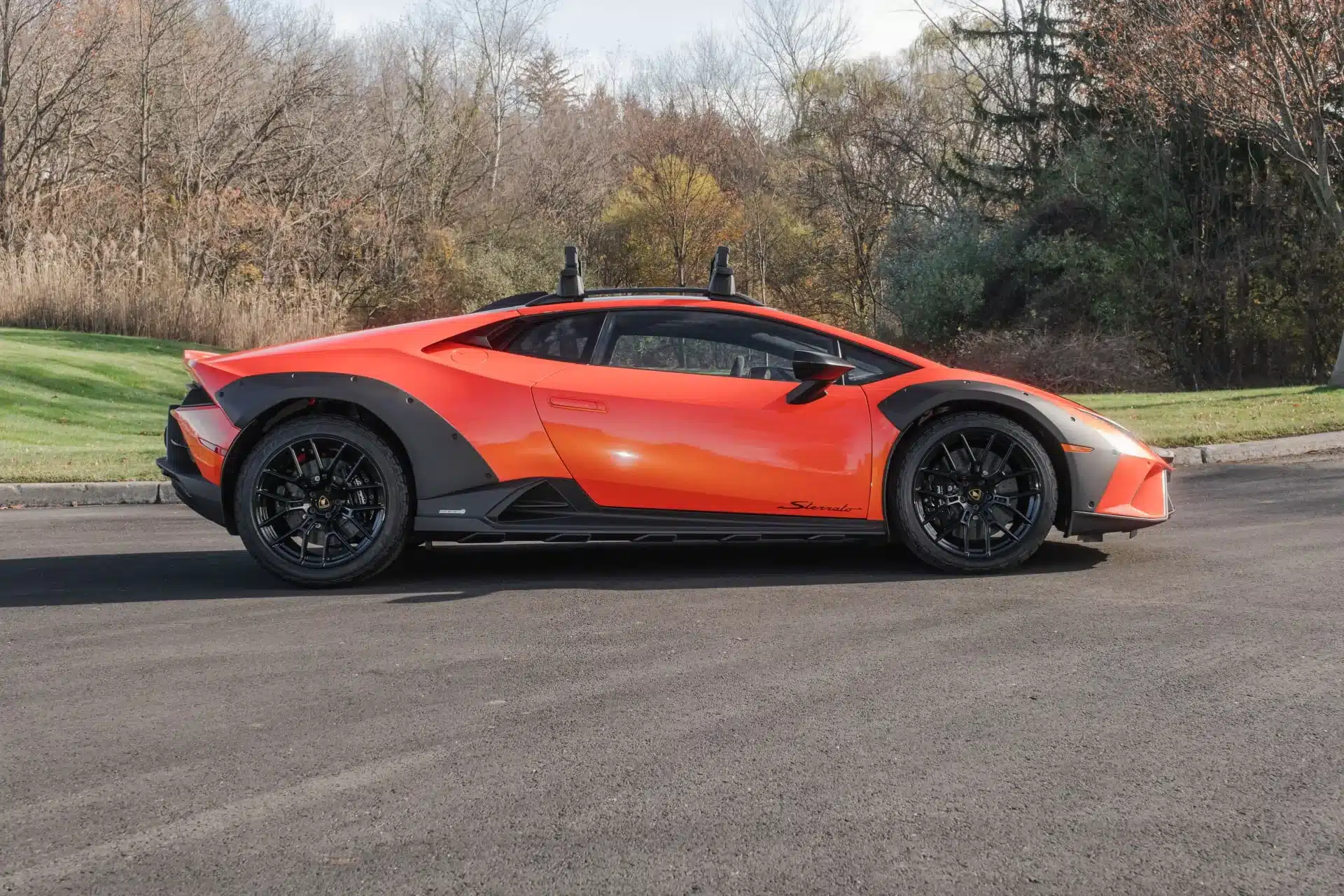 Seitenansicht eines Lamborghini Huracán Sterrato in leuchtendem Orange auf einer asphaltierten Straße, mit schwarzen Offroad-Details und erhöhtem Fahrwerk.