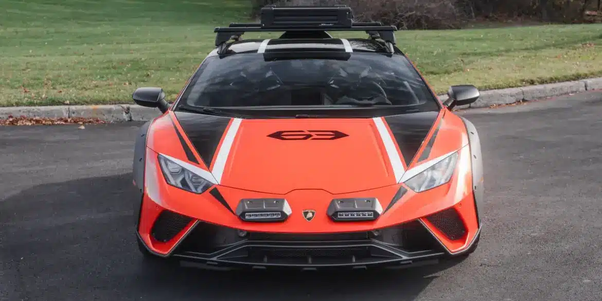Frontansicht eines orangefarbenen Lamborghini Huracán Sterrato mit Offroad-Elementen auf einem asphaltierten Parkplatz.