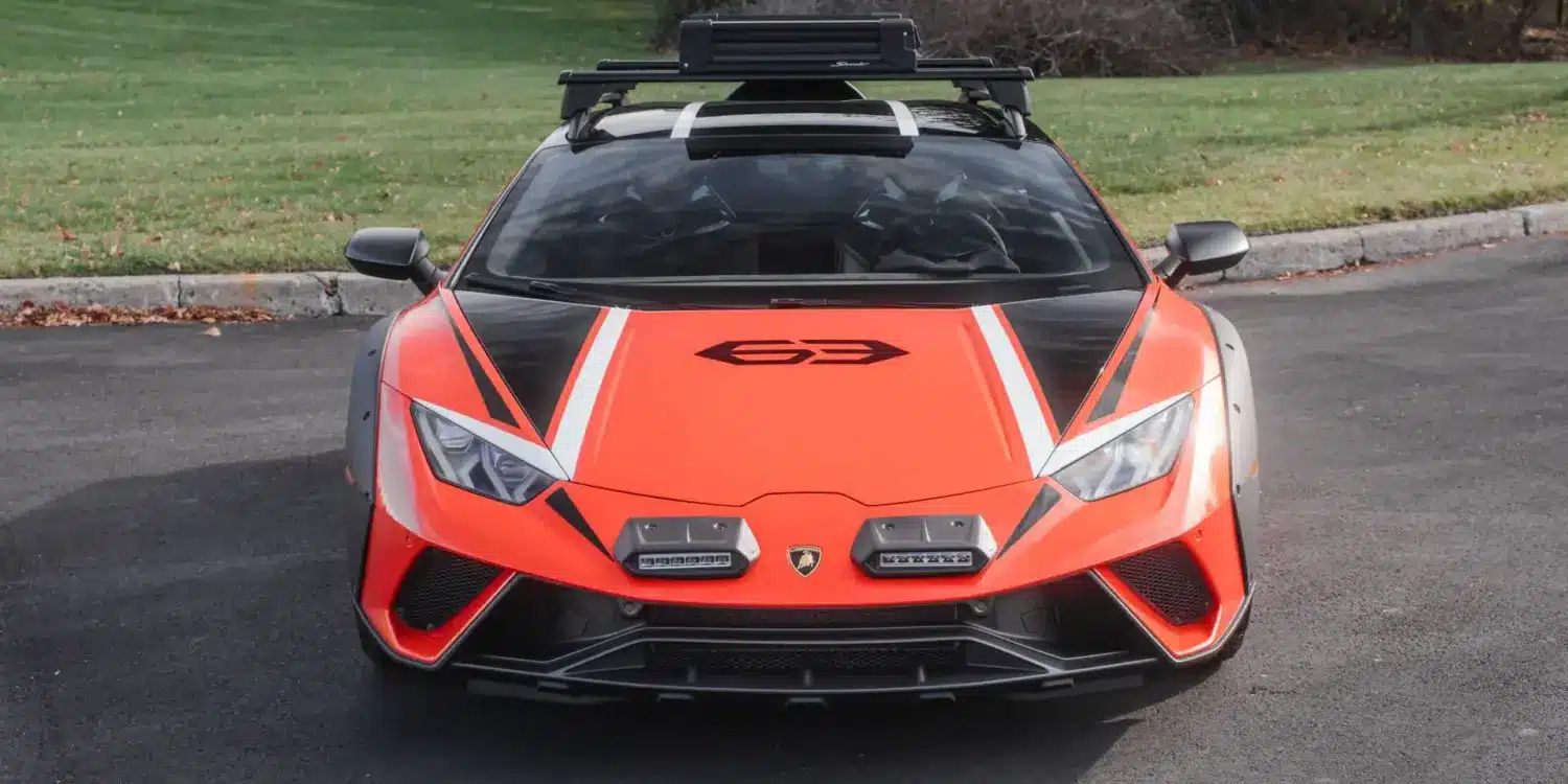 Frontansicht eines orangefarbenen Lamborghini Huracán Sterrato mit Offroad-Elementen auf einem asphaltierten Parkplatz.