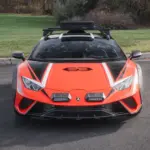 Frontansicht eines orangefarbenen Lamborghini Huracán Sterrato mit Offroad-Elementen auf einem asphaltierten Parkplatz.