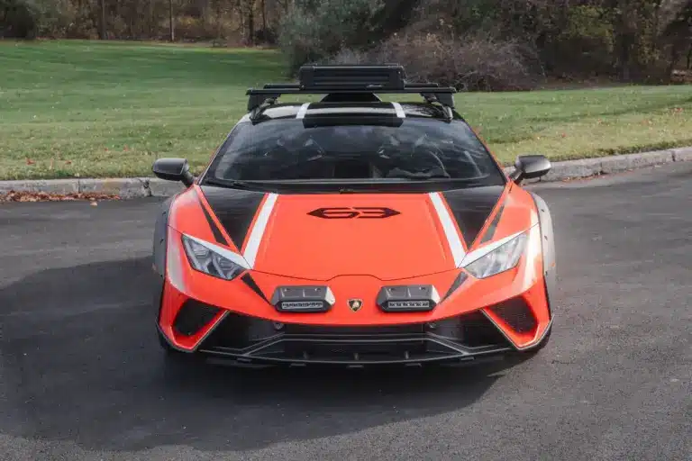 Frontansicht eines orangefarbenen Lamborghini Huracán Sterrato mit Offroad-Elementen auf einem asphaltierten Parkplatz.