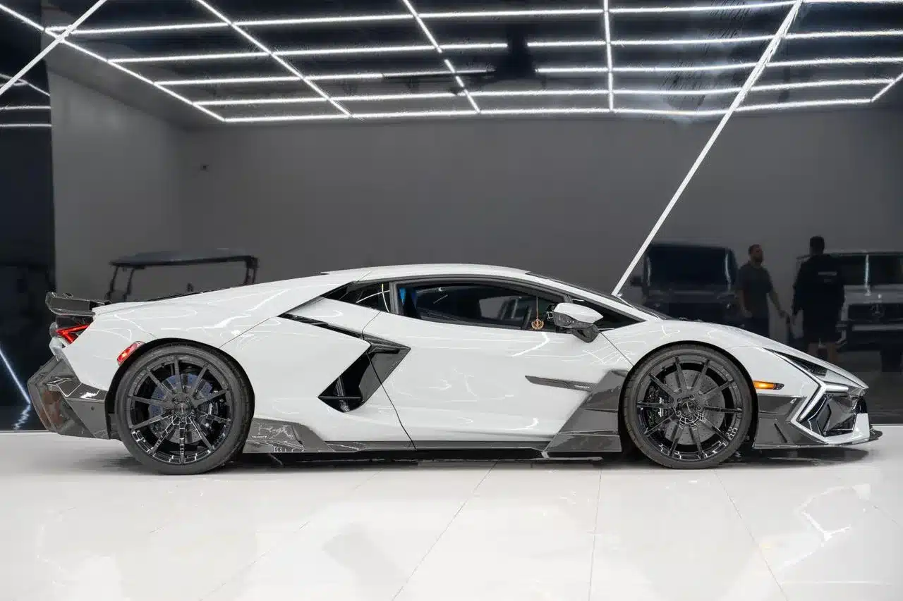 Seitenansicht eines weißen Lamborghini Revuelto Mansory 2025 mit Carbon-Elementen in einer modernen, hell ausgeleuchteten Garage.