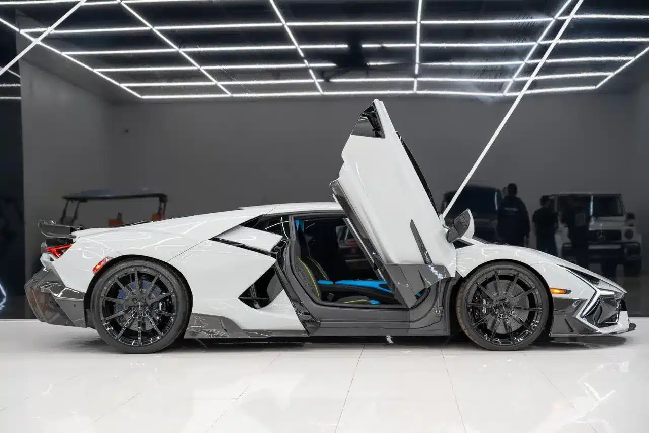 Lamborghini Revuelto Mansory 2025 in Weiß mit sichtbaren Carbon-Anbauteilen und geöffneten Flügeltüren, seitlicher Blick im Showroom.