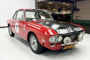 Lancia Fulvia Coupé Rallye 1.3S in Rot mit schwarzer Motorhaube und Zusatzscheinwerfern im Ausstellungsraum.