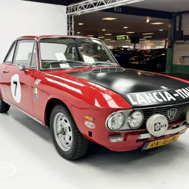 Lancia Fulvia Coupé Rallye 1.3S in Rot mit schwarzer Motorhaube und Zusatzscheinwerfern im Ausstellungsraum.