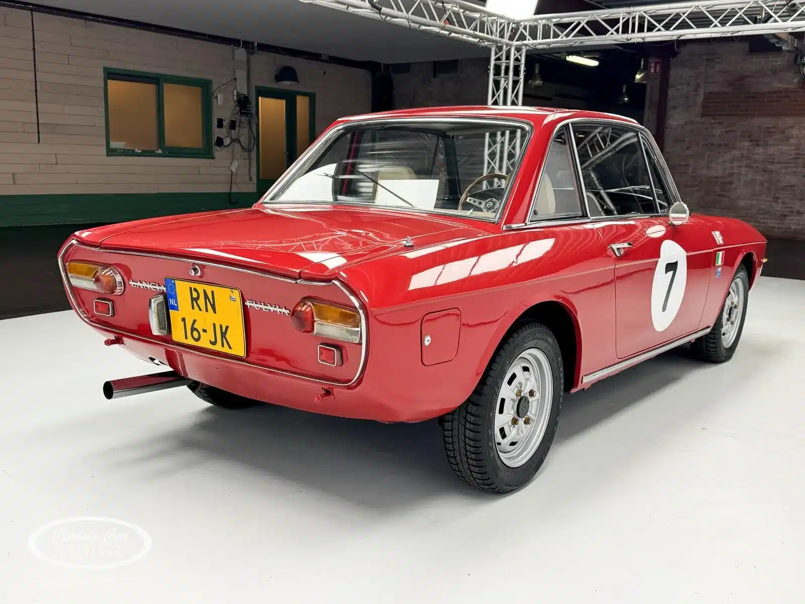 Heckansicht eines roten Lancia Fulvia Coupé Rallye 1.3S von 1974 mit Startnummer 7, goldfarbenen Felgen und niederländischem Kennzeichen.