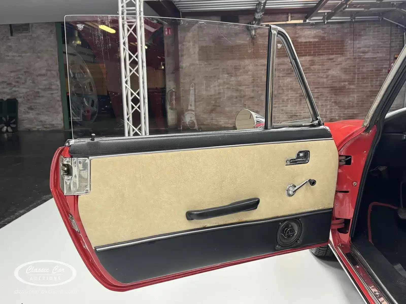 Geöffnete Fahrertür der Lancia Fulvia Coupé Rallye 1.3S mit beiger und schwarzer Türverkleidung, Fensterkurbel und Lautsprecher.