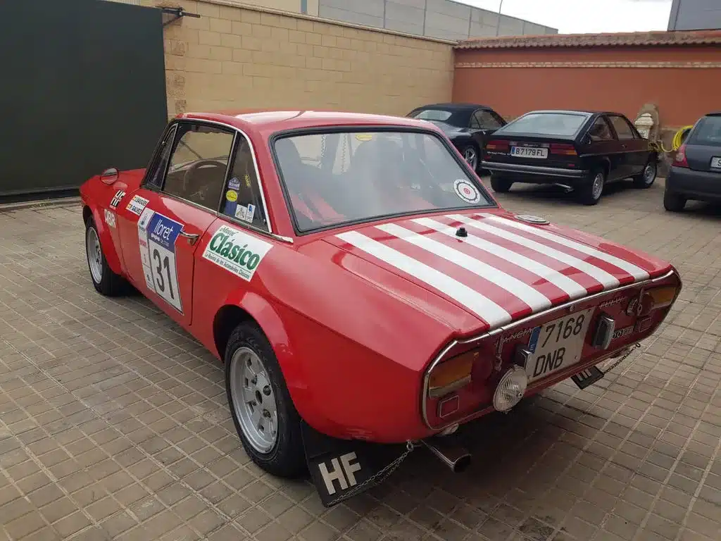 Lancia Fulvia HF 1600 Corsa in Rot mit weißen Rallyestreifen und Startnummer 31, geparkt vor einer Mauer