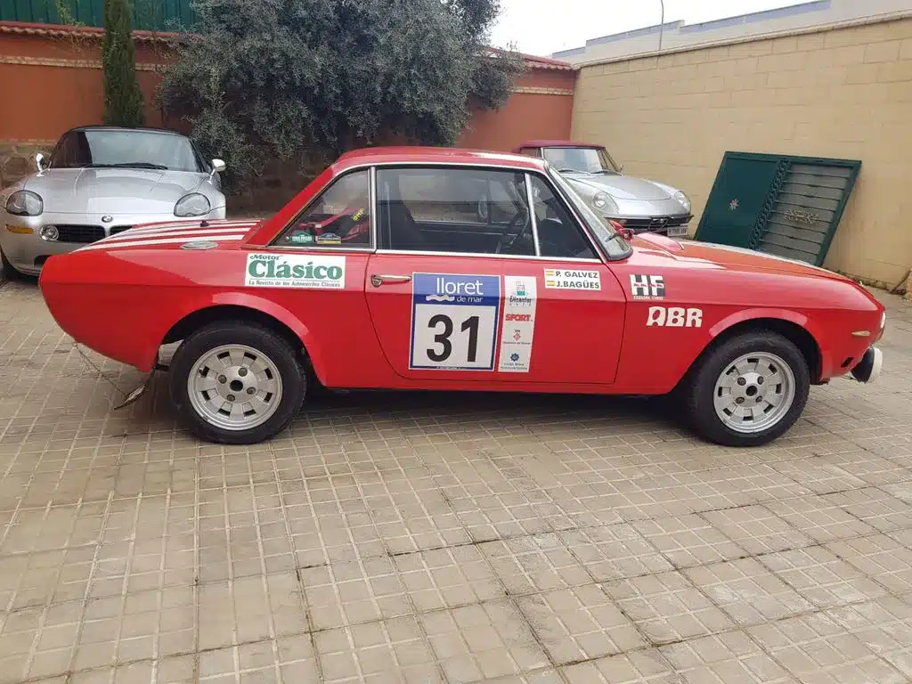 Lancia Fulvia HF 1600 Corsa, rot, mit Rallyebeschriftung und Startnummer, seitlich fotografiert.
