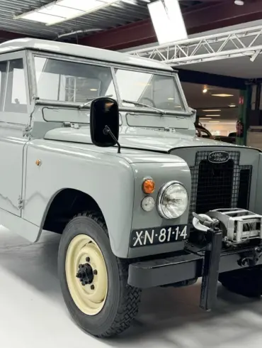 Restaurierter Land Rover Series II Baujahr 1968 mit grauer Lackierung und Kennzeichen XN-81-14, frontal aufgenommen in einer Ausstellungshalle.