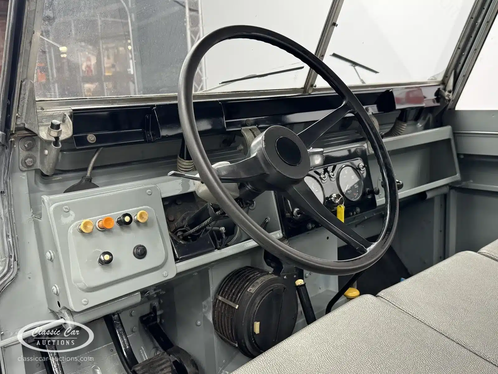 Innenansicht des Armaturenbretts und Lenkrads eines grauen Land Rover Series II von 1968, restaurierter Zustand, Fokus auf die Technik.
