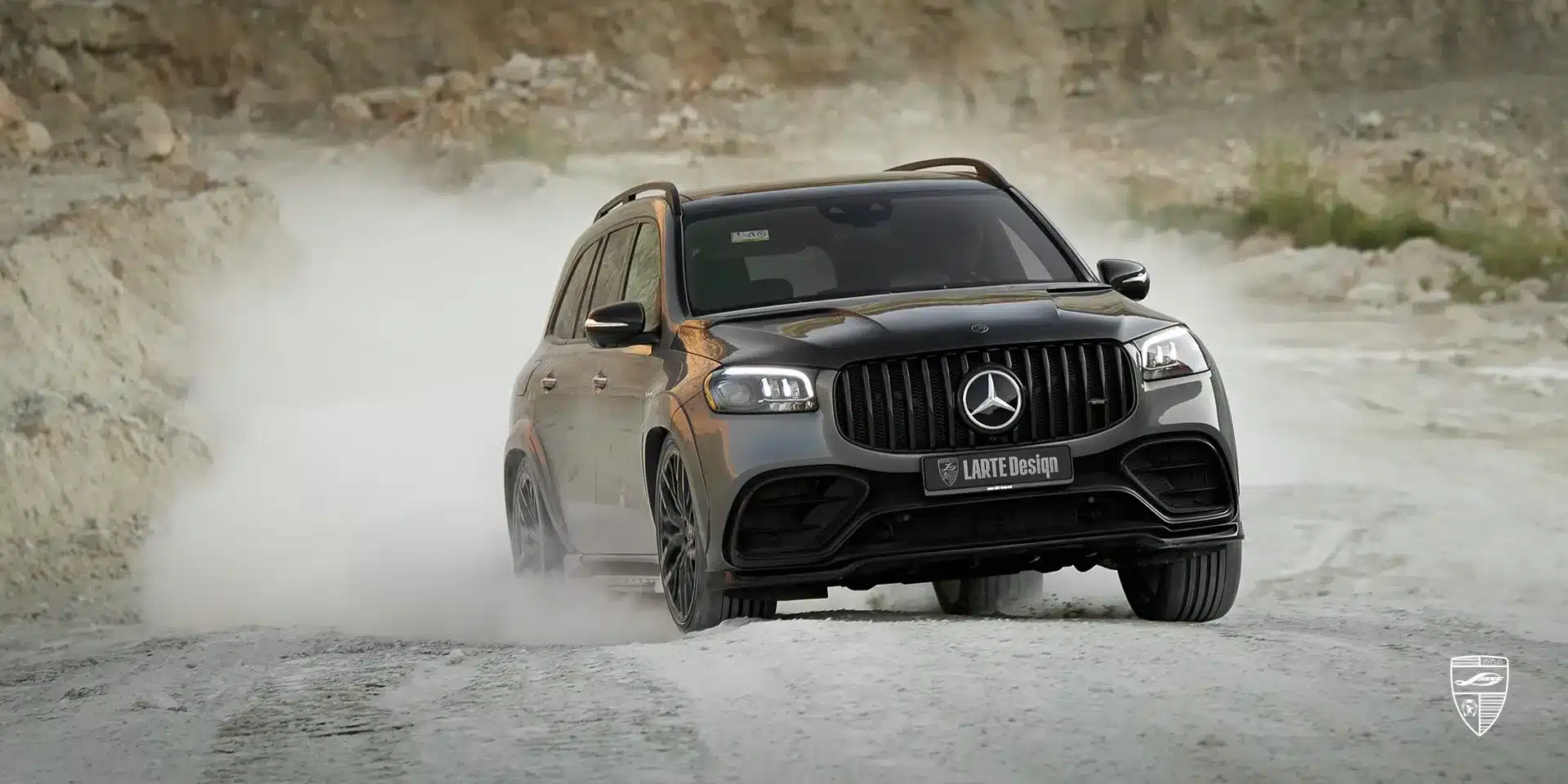 Ein Mercedes-AMG GLS 63 LARTE mit Carbon-Karosseriekit fährt dynamisch auf einer staubigen Piste vor felsiger Kulisse.