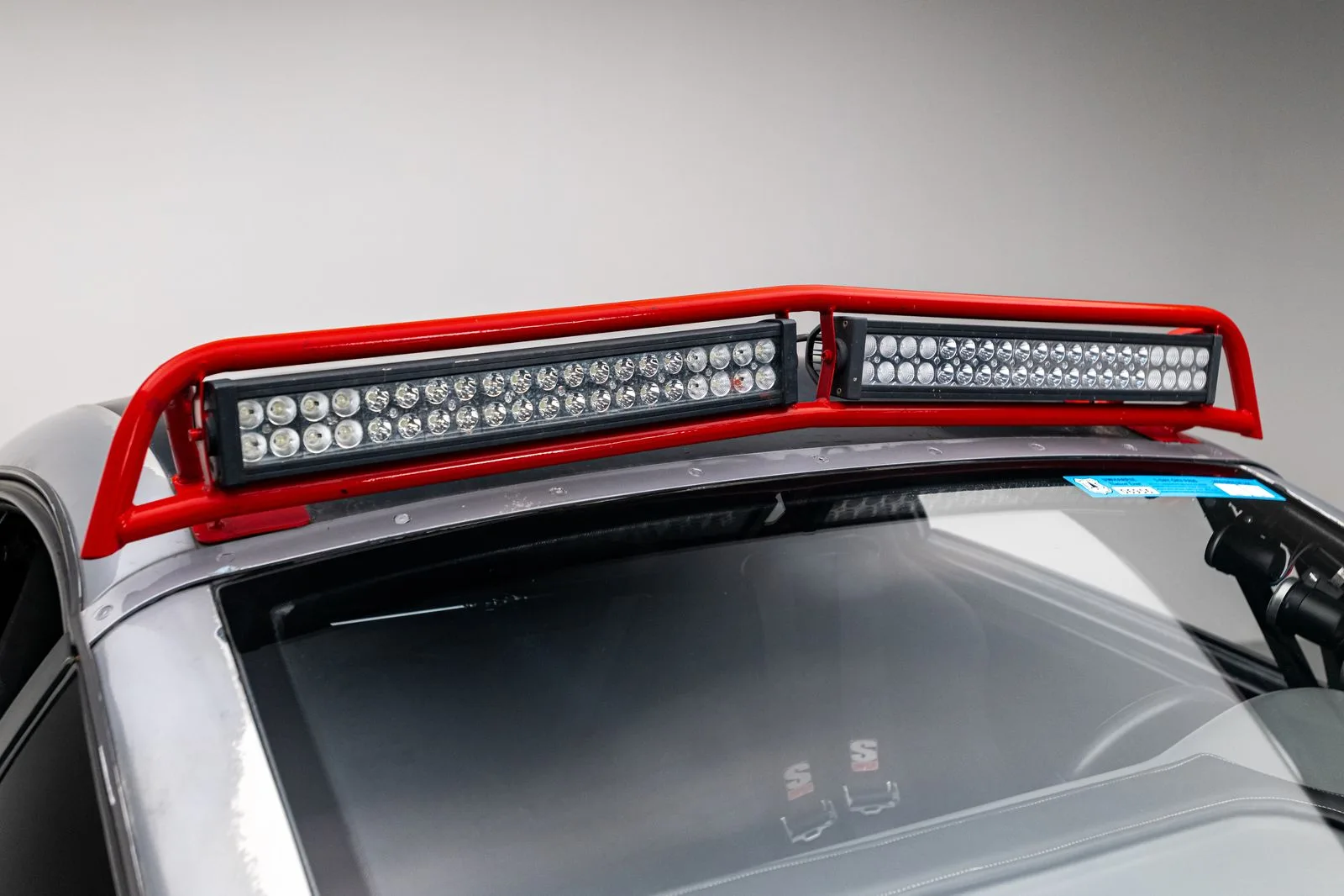 Roter Überrollbügel mit zwei LED-Lichtbalken auf dem Dach eines silbernen Offroad-Fahrzeugs, Detailaufnahme.