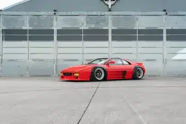 Liberty Walk LB-Works Ferrari 348TS, Baujahr 1990, in Rot und mit verbreiterten Kotflügeln vor einer Industriehalle.