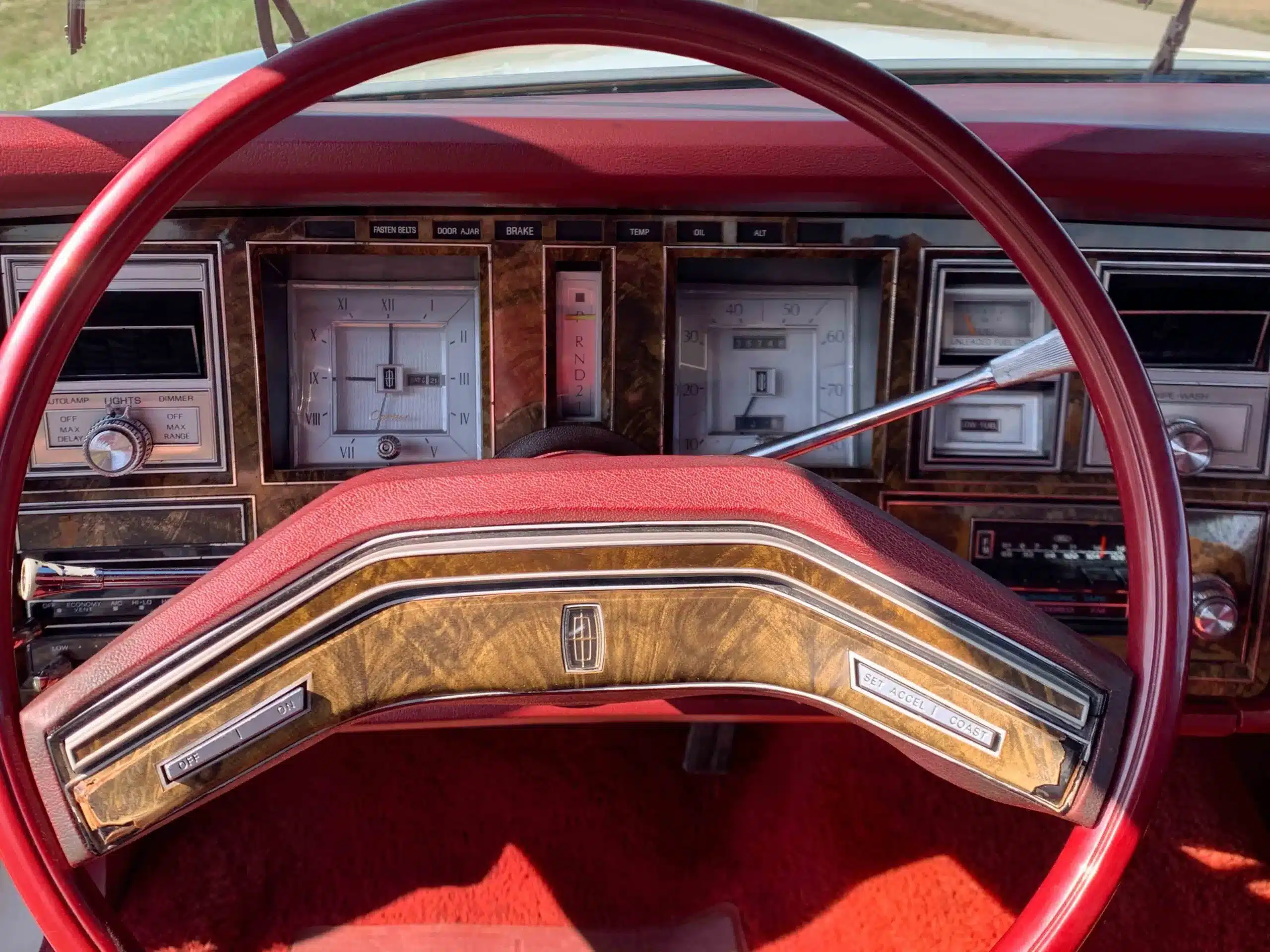 Innenansicht des Armaturenbretts und Lenkrads im Lincoln Continental MK V von 1977, mit roten Polstern und Holzeinlagen.
