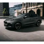 Grauer Maserati Grecale Folgore 2026 vor moderner Glasfassade, seitliche Ansicht.