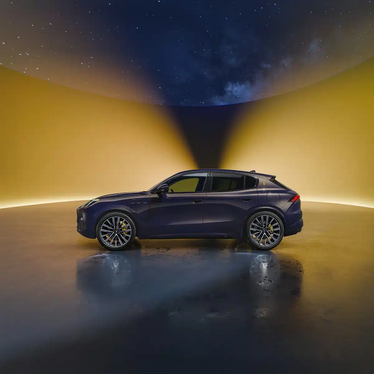 Seitliche Ansicht des Maserati Grecale Lumina Blu in dunkler Metallic-Lackierung, stehend vor einem gelb ausgeleuchteten Hintergrund