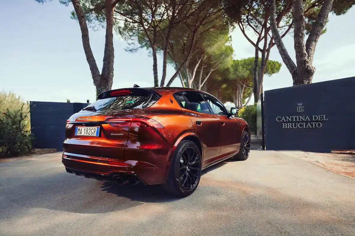 Roter Maserati Grecale Tributo Il Bruciato parkt vor dem Tor der Cantina del Bruciato, umgeben von Bäumen und mediterraner Landschaft.