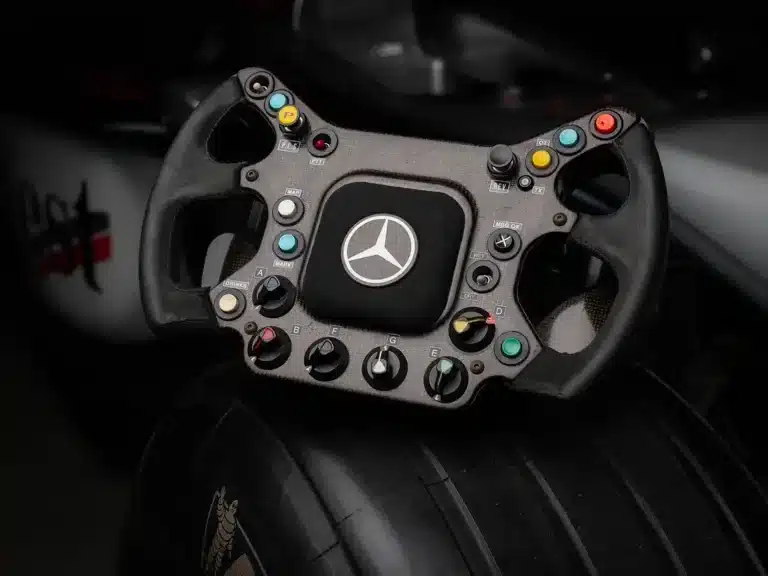 Formel-1-Lenkrad des McLaren MP4‑17A mit Mercedes-Benz-Logo und zahlreichen Bedienelementen, auf einem Slick-Reifen abgelegt.