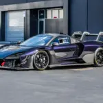 Seitliche Ansicht eines McLaren Senna GTR in dunklem Violett mit markantem Heckflügel und Rennsportdetails, geparkt vor einem modernen Industriegebäude.