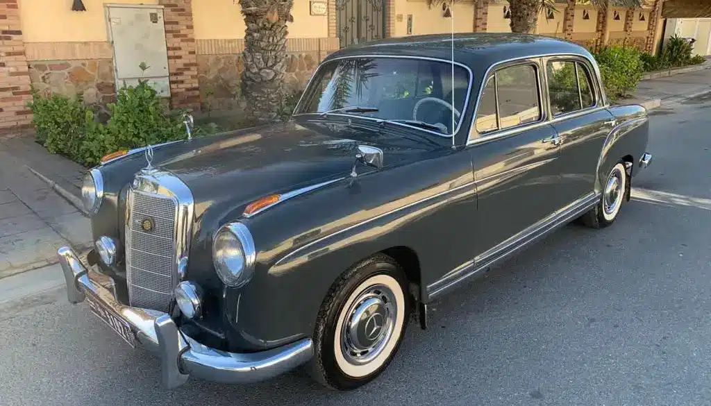Mercedes-Benz 220 S Ponton Limousine, dunkelgrau, Baujahr 1950er, geparkt an einer Straße unter Palmen.