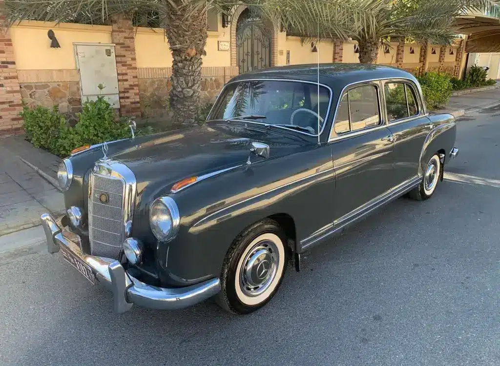 Mercedes-Benz 220 S Ponton Limousine, dunkelgrau, Baujahr 1950er, geparkt an einer Straße unter Palmen.