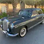 Mercedes-Benz 220 S Ponton Limousine, dunkelgrau, Baujahr 1950er, geparkt an einer Straße unter Palmen.
