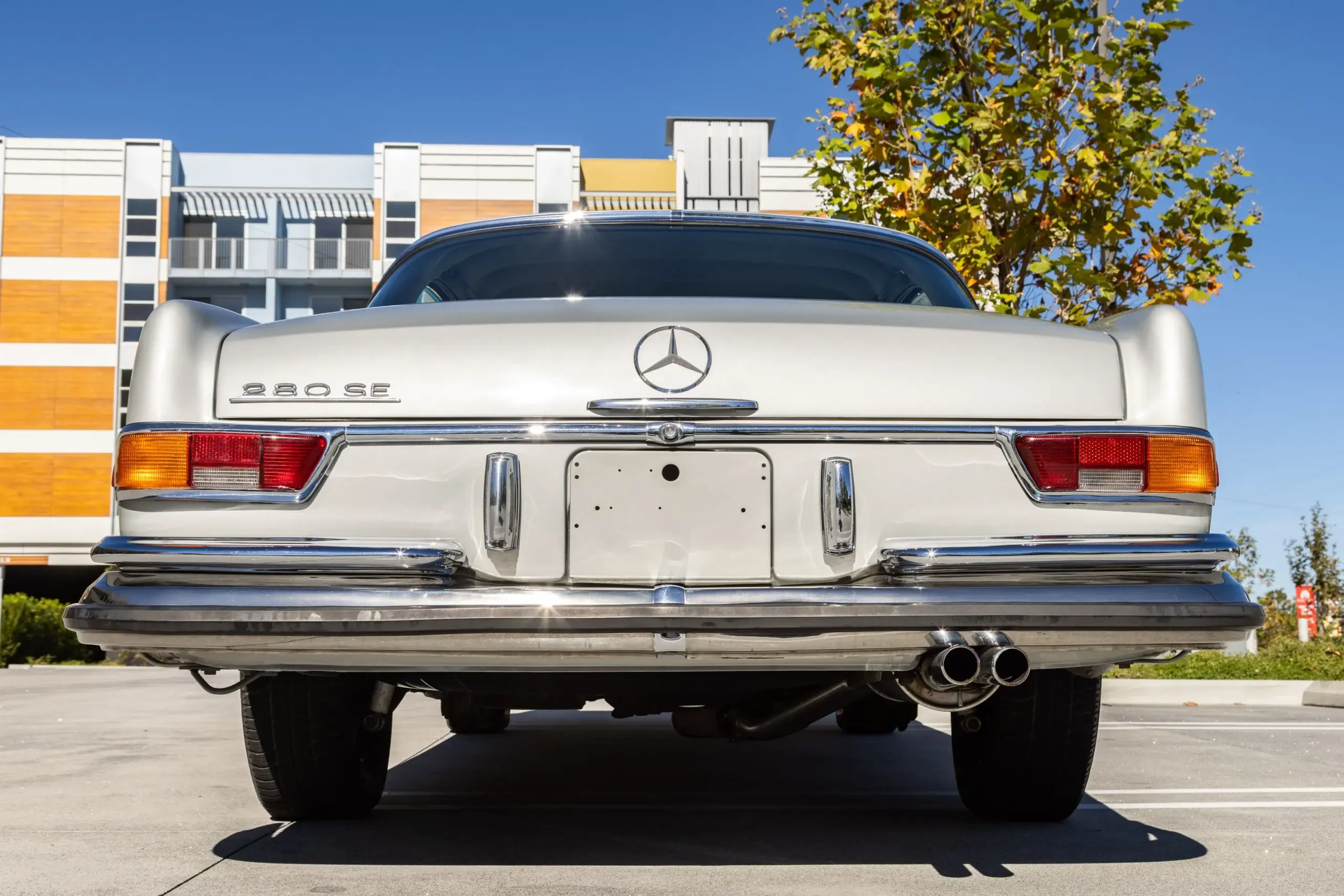Heckansicht eines silbergrauen Mercedes-Benz 280SE Coupé W111 mit Chromstoßstange und Doppelauspuff, Baujahr 1970.