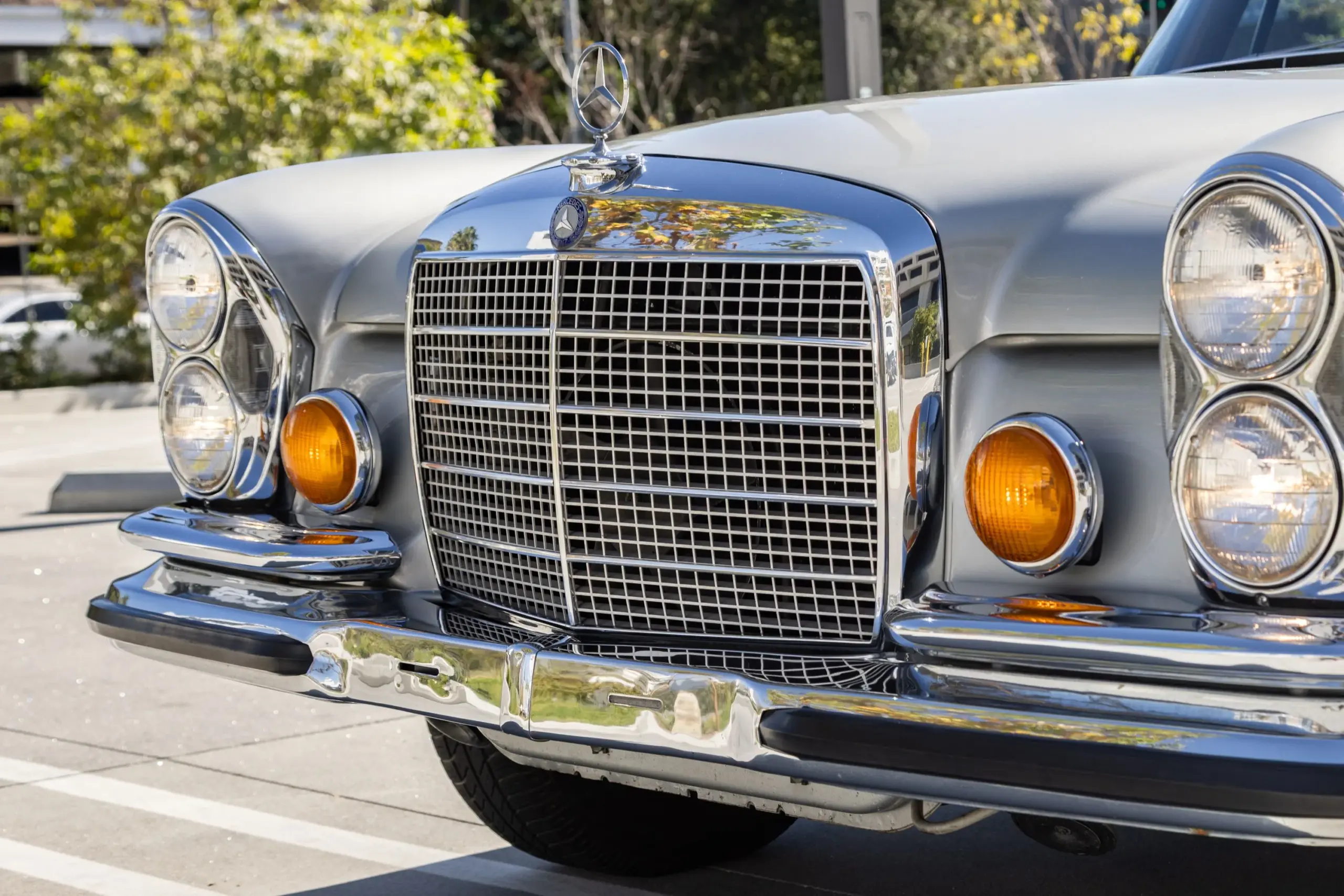 Der verchromte Frontgrill und die Doppelscheinwerfer eines silbergrauen Mercedes-Benz 280SE W111 Coupés aus dem Jahr 1970.