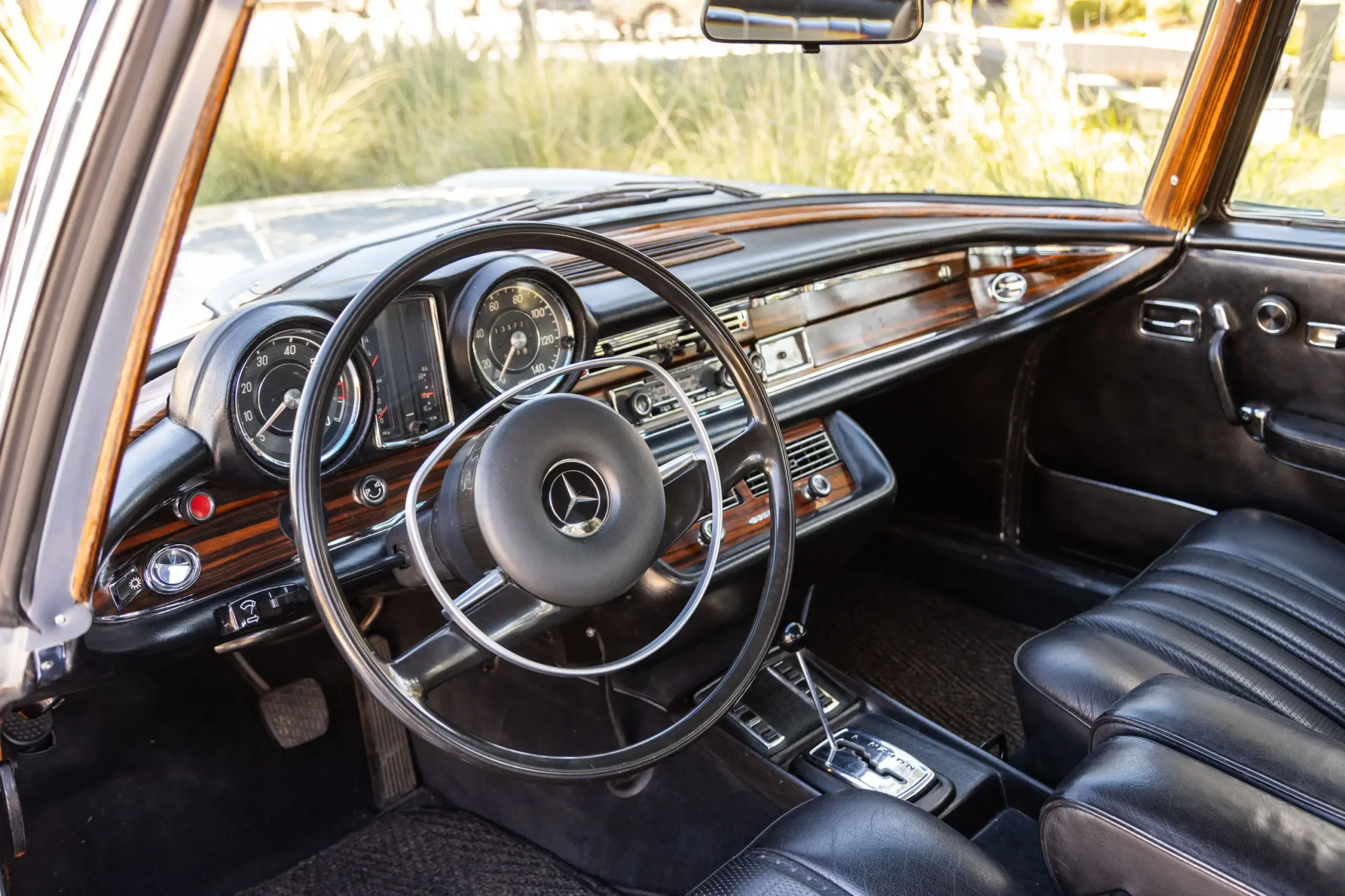 Innenraum eines Mercedes-Benz 280SE W111 Coupé mit schwarzem Leder, Holzarmaturenbrett und klassischen Instrumenten