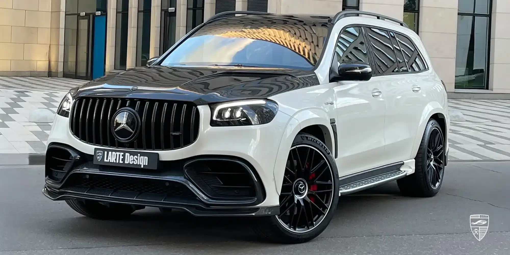 Mercedes-Benz GLS 63 AMG X167 mit LARTE Design Winner Bodykit, Carbon-Motorhaube und 23-Zoll-Rädern, frontal abgebildet vor moderner Architektur.