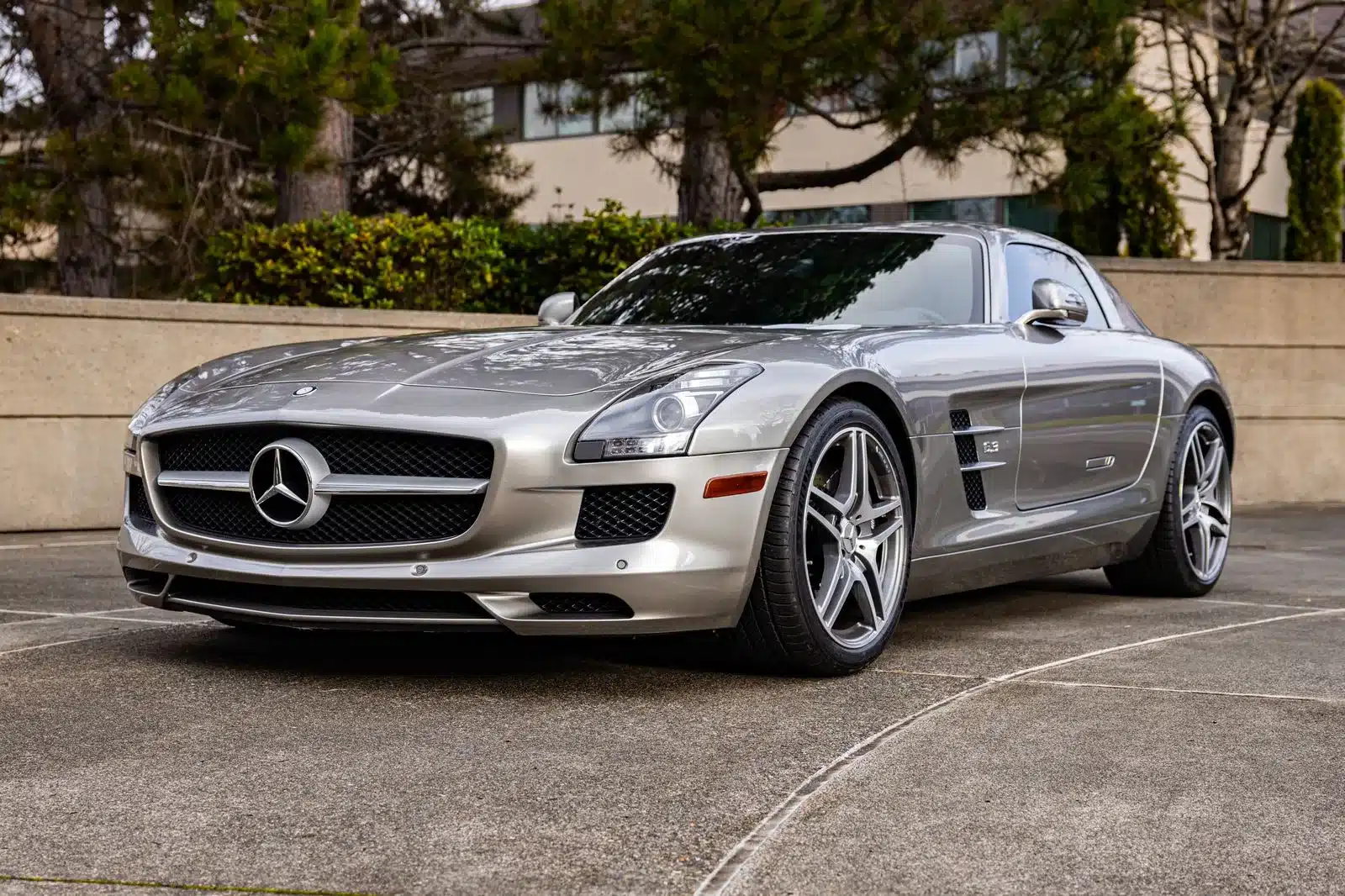 Mercedes-Benz SLS AMG Gullwing in Alubeam-Silber, seitlich frontal fotografiert auf einem Parkplatz, betont die klaren Linien der Karosserie.
