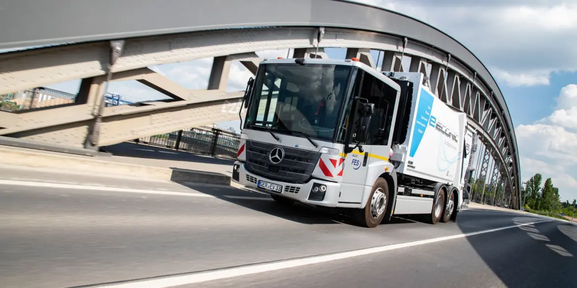 Elektrischer Lkw Mercedes-Benz eEconic fährt über eine Brücke in einer urbanen Umgebung.