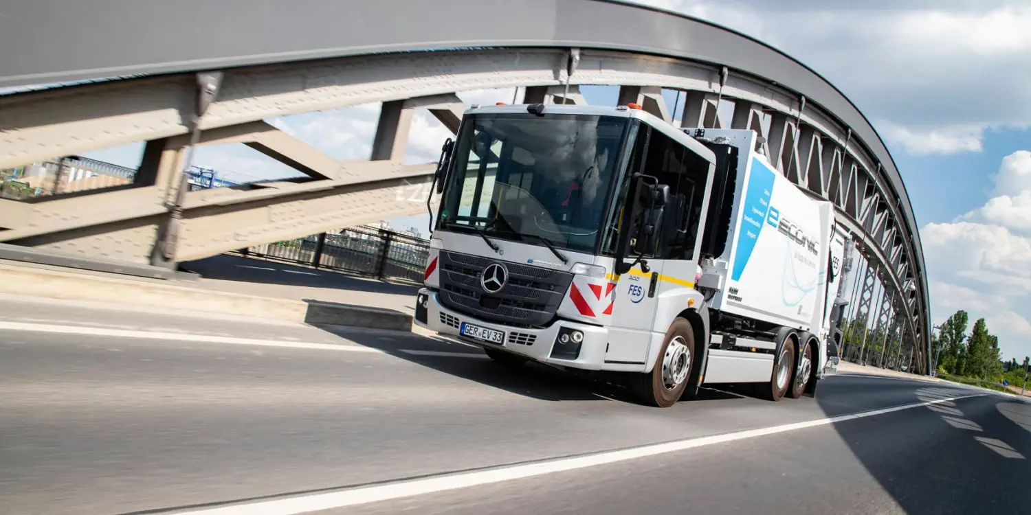 Elektrischer Lkw Mercedes-Benz eEconic fährt über eine Brücke in einer urbanen Umgebung.