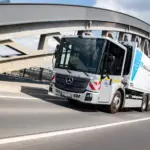 Elektrischer Lkw Mercedes-Benz eEconic fährt über eine Brücke in einer urbanen Umgebung.